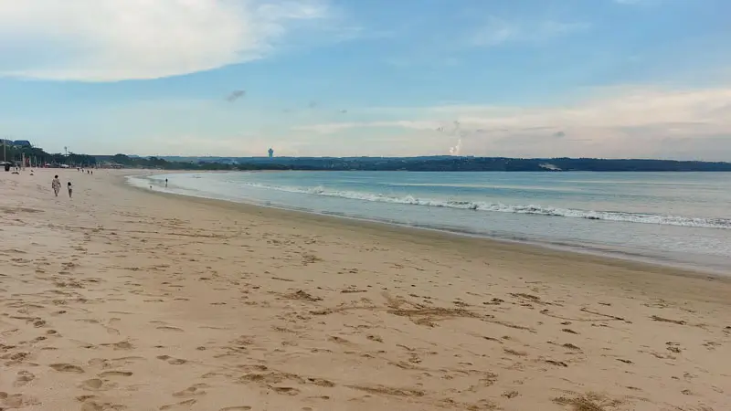 Wide view of Jimbaran Beach Bali on a sunny afternoon with gentle waves. © Wira Tour