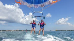 Two smiling guests parasailing over the calm sea in Tanjung Benoa, Bali