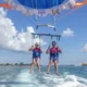 Two smiling guests parasailing over the calm sea in Tanjung Benoa, Bali