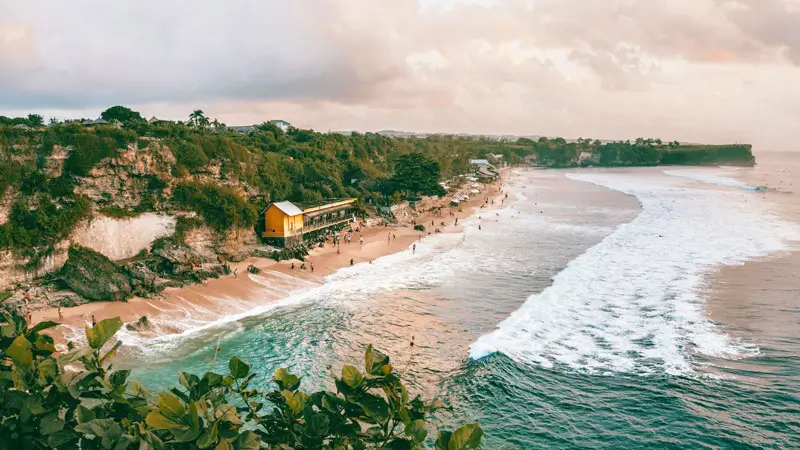 Cliffside view of Balangan Beach Bali at golden hour with soft light and reef waves.