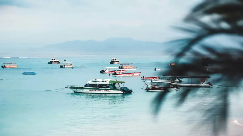 Fast boats anchored off Jungutbatu beach with clear water and mountain backdrop