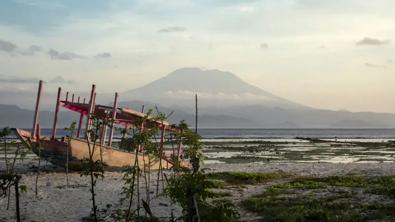 View of Mount Agung from Nusa Lembongan with a wooden boat on the shoreline