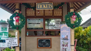 Penglipuran ticket counter with price board and hours sign 08:00–18:30 WITA