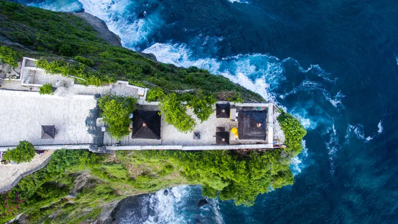 Aerial view of a cliffside temple and ocean walkway in Pecatu, Bali