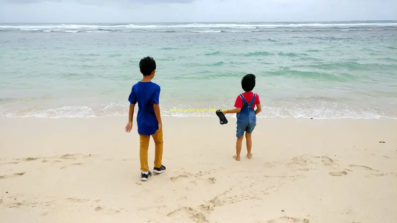 Children at Melasti Beach gentle shoreline; swim inside red-yellow flags.