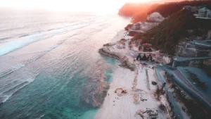 Aerial view of Melasti’s limestone cliffs, S-curve access road, and turquoise bay at sunset afterglow