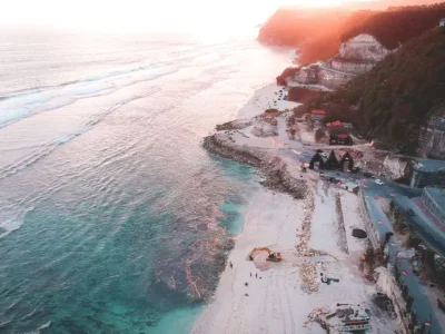 Aerial view of Melasti’s limestone cliffs, S-curve access road, and turquoise bay at sunset afterglow