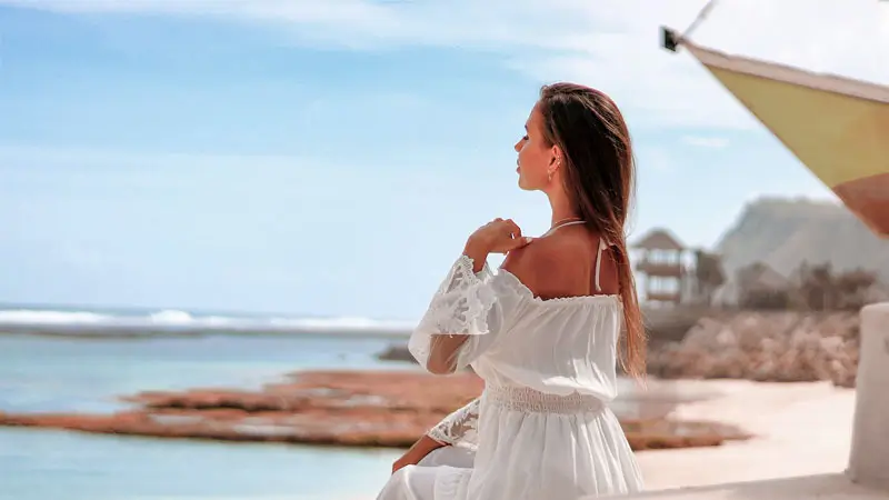Traveler seated on seawall steps with tide pools and turquoise water in background