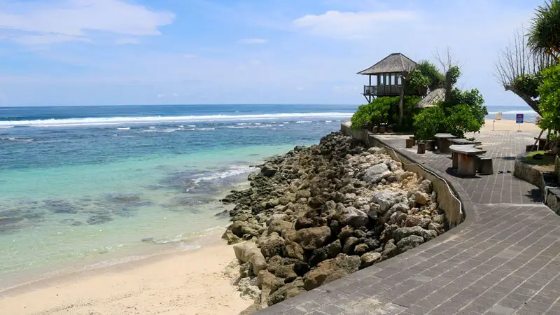Rocky shoreline beside paved path at Melasti public beach; watch footing, water shoes help.
