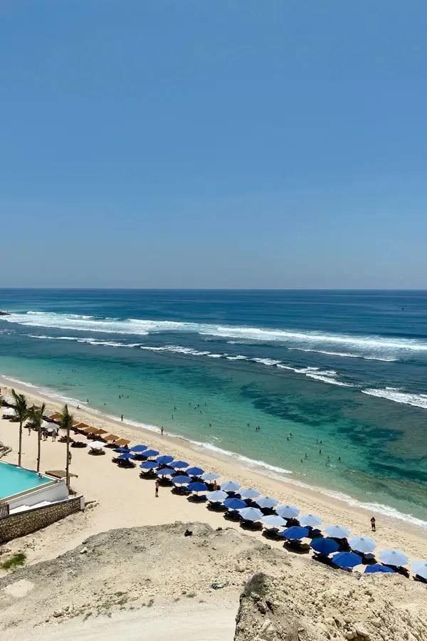 Rows of beach umbrellas on shoreline area with gentle nearshore, bluff view.