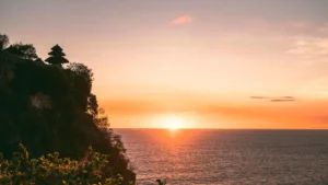 Uluwatu cliff at sunset with temple silhouette over the ocean.