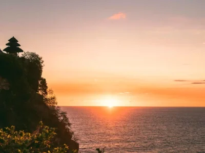 Uluwatu cliff at sunset with temple silhouette over the ocean.