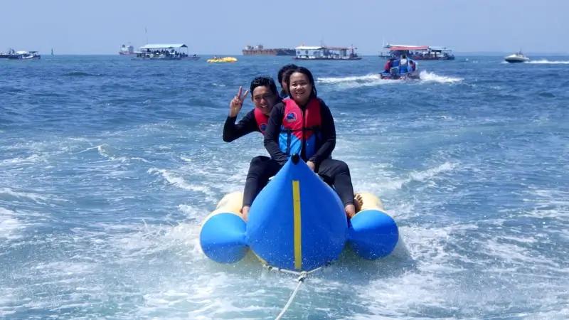 Two riders towed on an inflatable raft, smiling and waving.