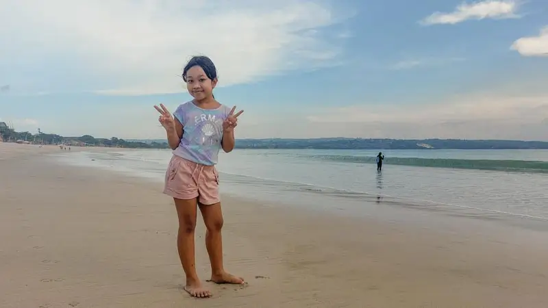 Girl posing on a wide, calm sandy beach with gentle waves