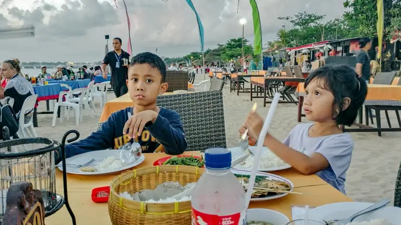 Children eating grilled seafood at a beachside table