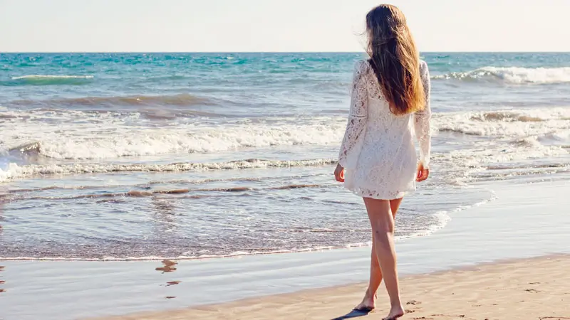 Woman in white dress walking alone on a quiet beach