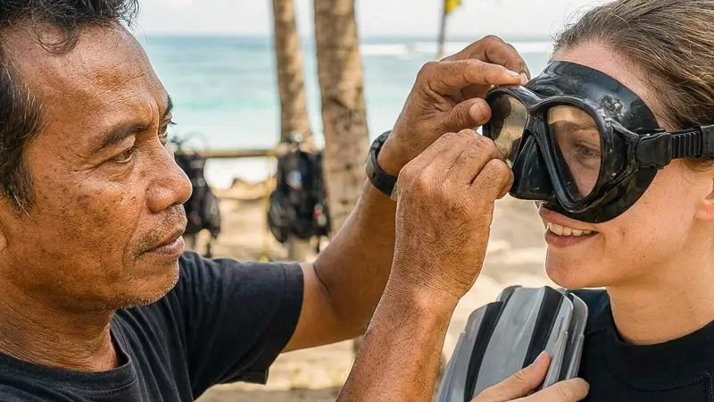 Instructor adjusts a beginner’s mask fit before entering the water for Discovery Scuba Diving