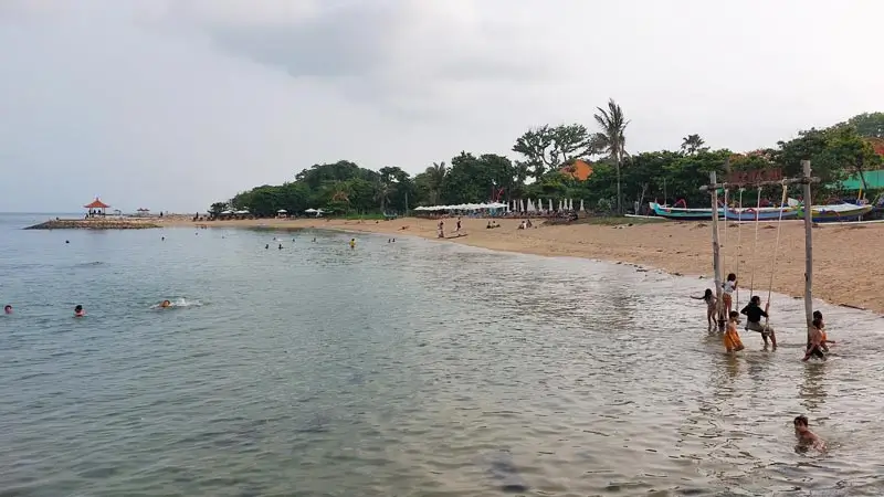 Sanur beach with calm water and people wading near shore