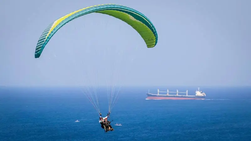 Tandem paragliding in Bali above the ocean, with a ship in the distance.