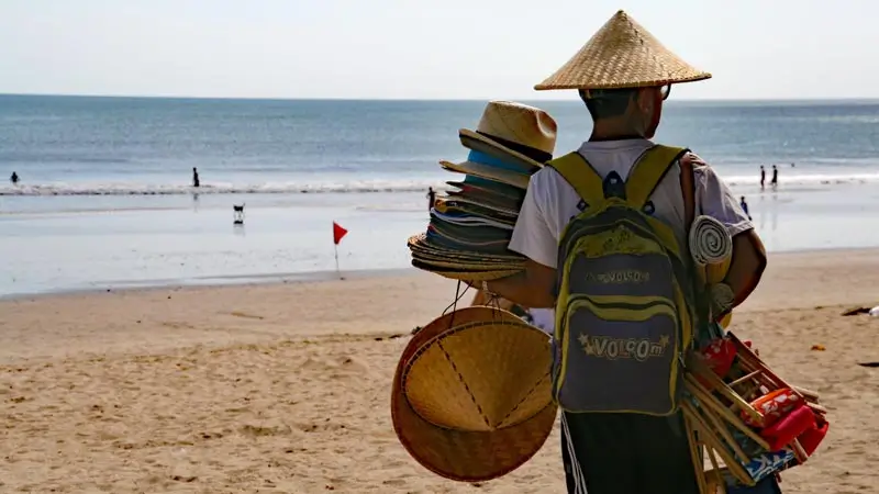 Vendor carrying hats along the sand in Bali