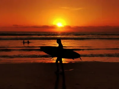 Surfer silhouette carrying a board at sunset on Legian Beach