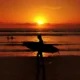 Surfer silhouette carrying a board at sunset on Legian Beach