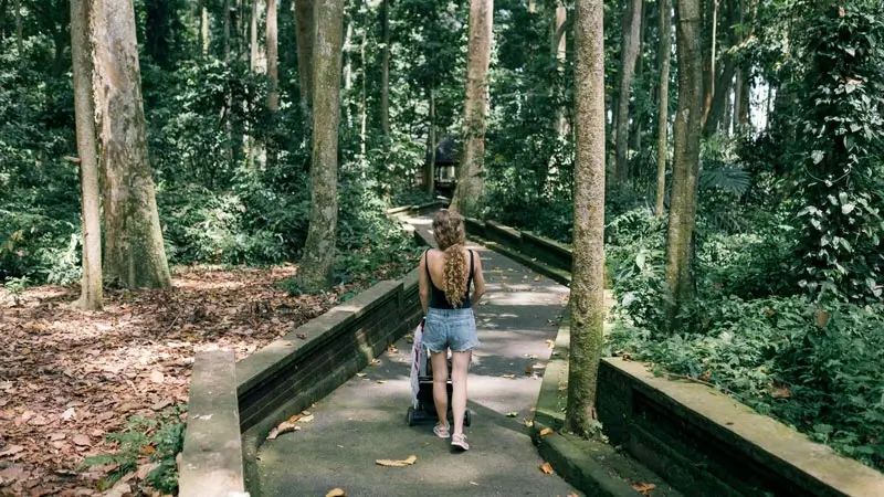 Parent pushing a stroller on a shaded path in Ubud